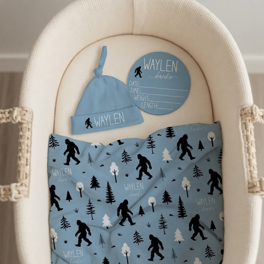 Personalized Bigfoot baby bundle with custom name swaddle hat and birth stat sign in bassinet, complete Sasquatch newborn gift set