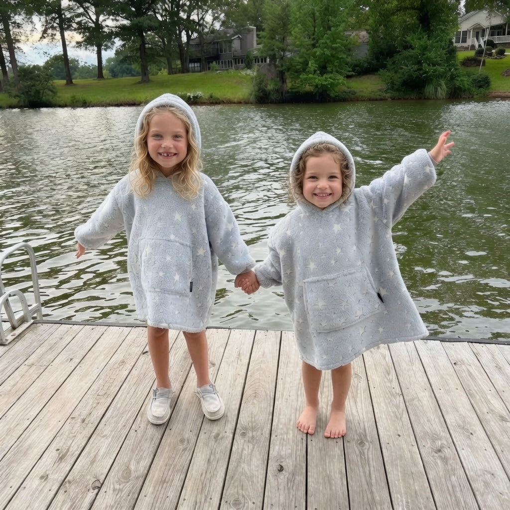Two children in glow hoodie standing on a wooden dock by a lake.