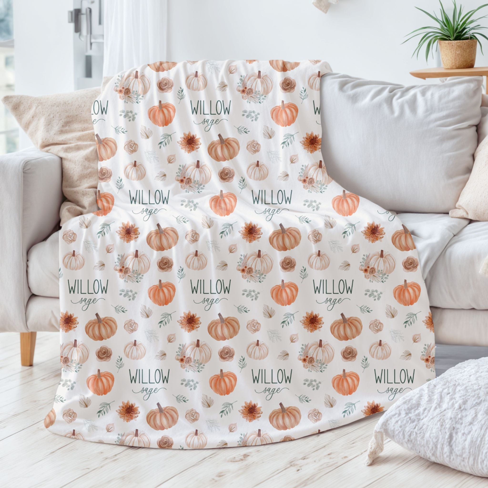 Personalized fall pumpkin blanket with watercolor pumpkins and florals draped over a gray couch with custom name Willow Sage from Twinklette